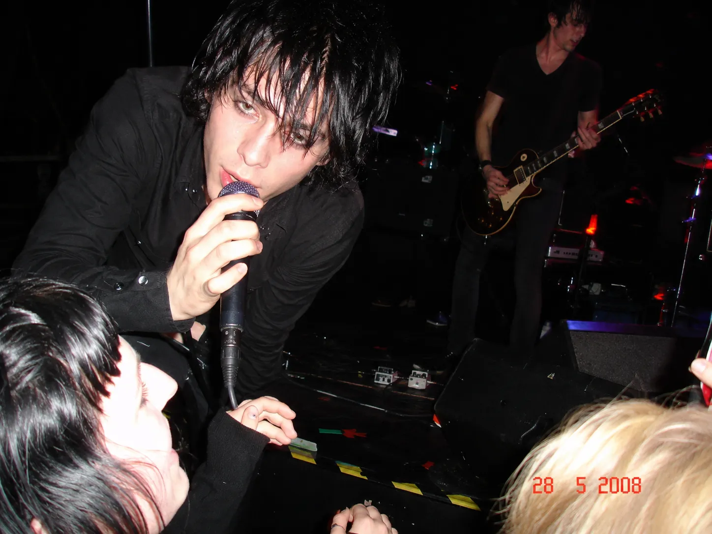 A singer reaching into the front row, frozen mid-motion against the stage behind him.