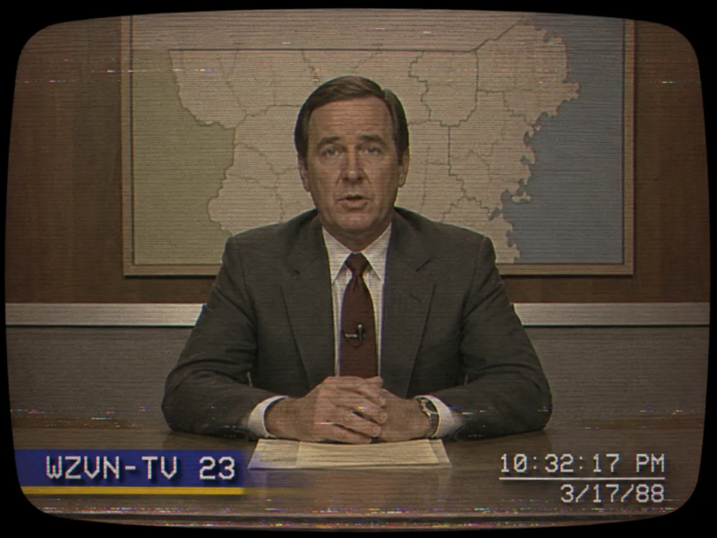 A presenter to camera, with the broadcast style holding the frame, the overlay and the picture damage together.